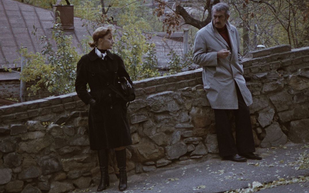 Film still from SOME INTERVIEWS ON PERSONAL MATTERS: A man and a woman stand leaning against a wall on the street and look at each other.