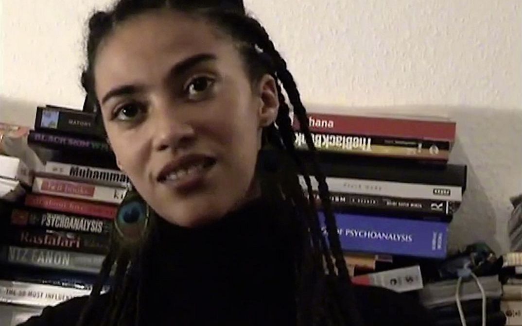 Still from the film "The Maji-Maji Readings" by Ricardo Barcallo. Close up of a women sitting in front of books