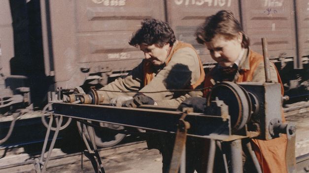 Film still from ORANGE VESTS: Two female workers in orange vests at work on a railroad track.