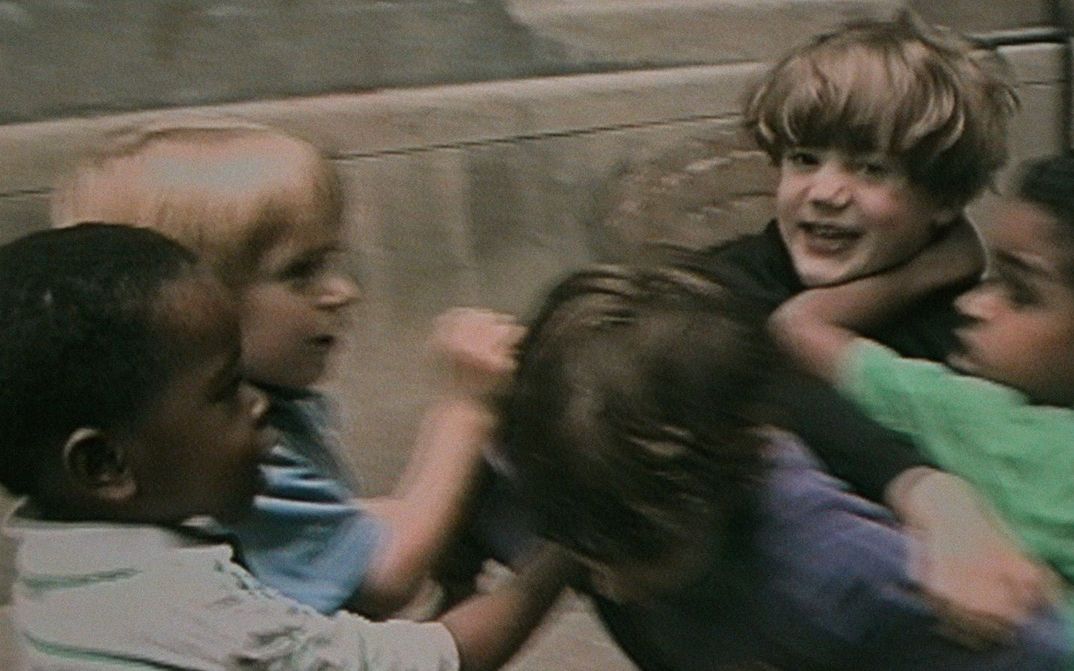 Film still from RÉCRÉATIONS: A group of children in a playful fight.