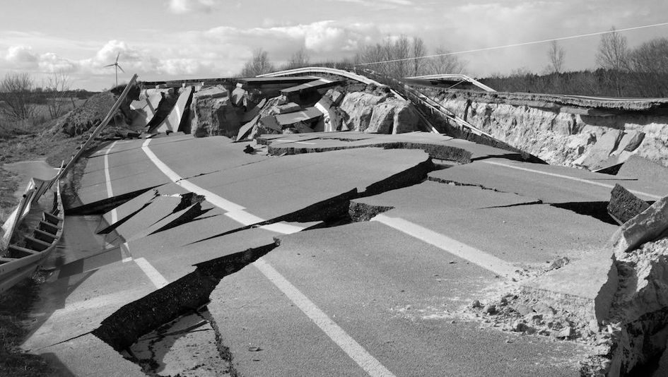 Film still from HEIMAT IST EIN RAUM AUS ZEIT: A completely torn up road. Bare trees and a wind turbine in the background.