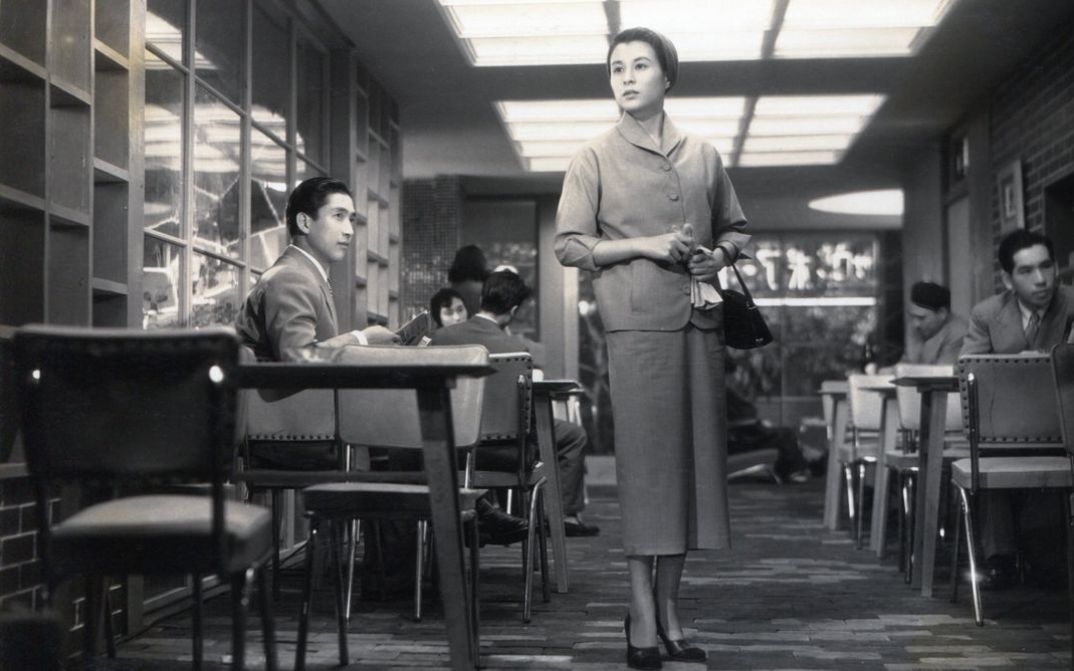 Film still from KOIBUMI: A woman stands in a pub and looks around searchingly.