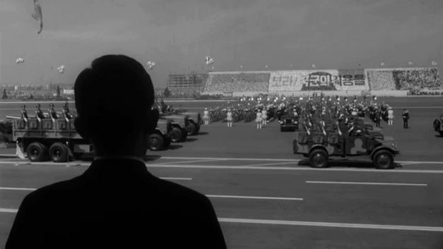 Filmstill aus THE SENSE OF VIOLENCE von Mooyung Kim. Das schwarz-weiße Bild zeigt eine Militärparade. Im Vordergrund ist die Silhouette einer Person.