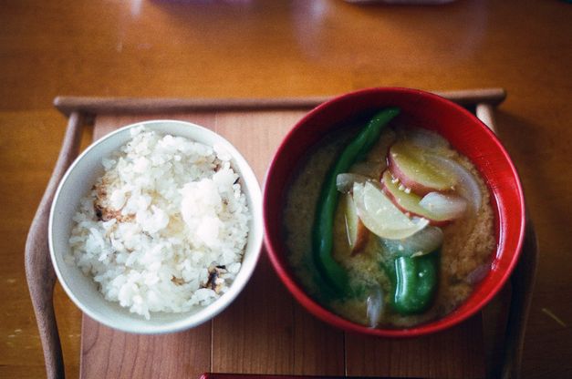 Draufsicht auf ein Tablett mit einer Schale Reis und einer Schale Suppe mit Gemüse auf einem Holztisch.