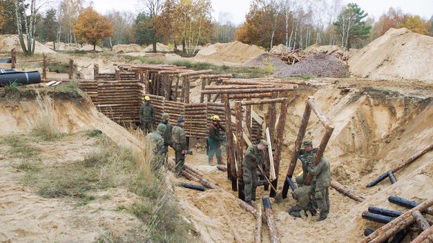 Soldaten bauen Holzbefestigungen in sandigem Gelände mit Werkzeugen.