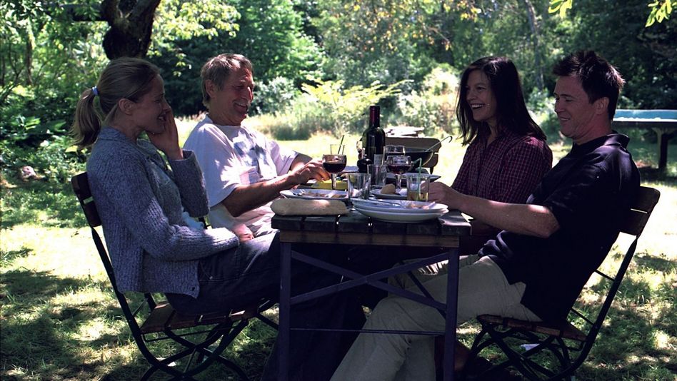 Two men and two women sit at a garden table set with wine and food and look happy.