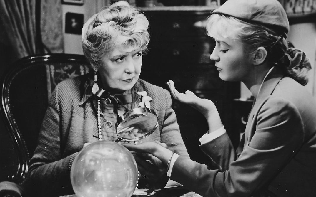 Film still from SOUS LE CIEL DE PARIS COULE LA SEINE: An older and a younger woman sit together at a table.