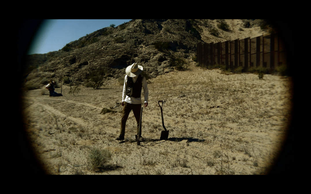 Filmstill aus TERRESTIAL SEA: Eine Person steht auf einem Feld und blickt zu Boden.