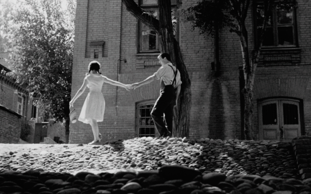 Film still from APRILI: Two young people hold hands on a cobbled street.