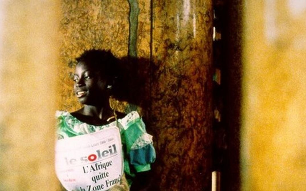 Film still from LA PETITE VENDEUSE DE SOLEIL: A girl stands on a corner with a copy of the newspaper "Le Soleil".
