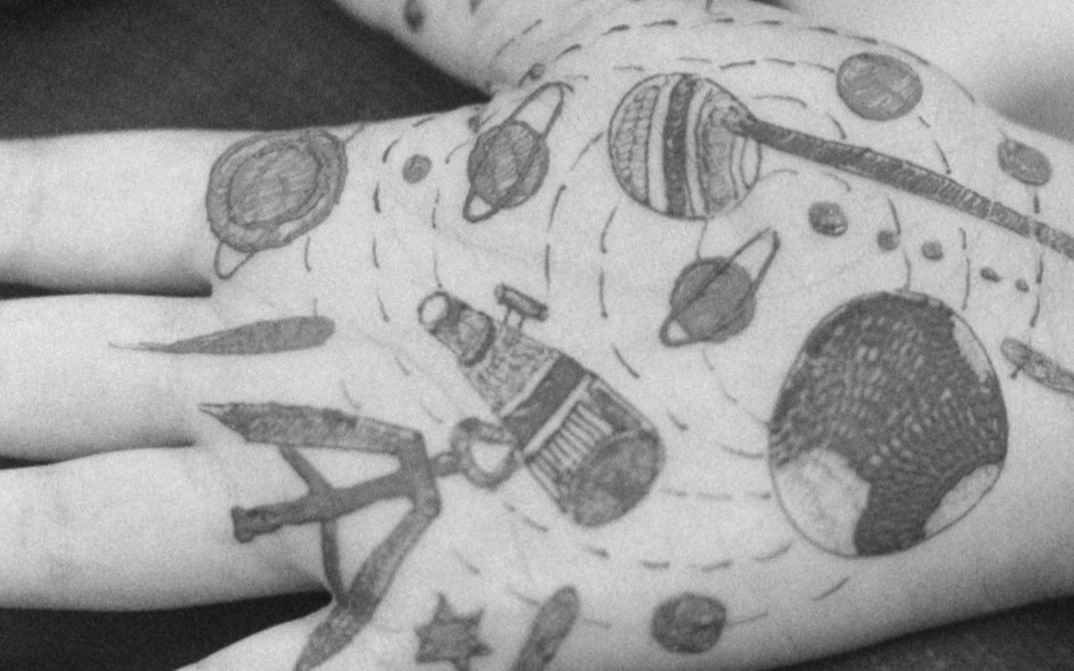 Filmstill aus dem Film „O Seeker“ von Gavati Wad. Eine Handfläche mit verschiedenen Illustrationen, darunter Planeten, Sterne und Linien.
