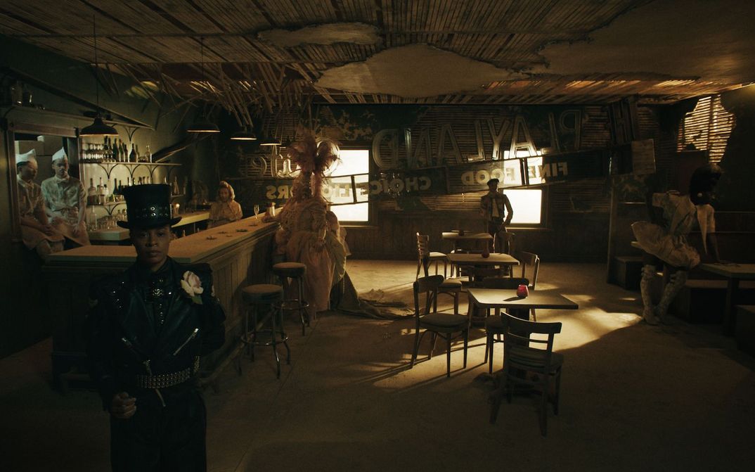 Film still from PLAYLAND: A row of people in imaginative costumes stand in an otherwise empty bar.