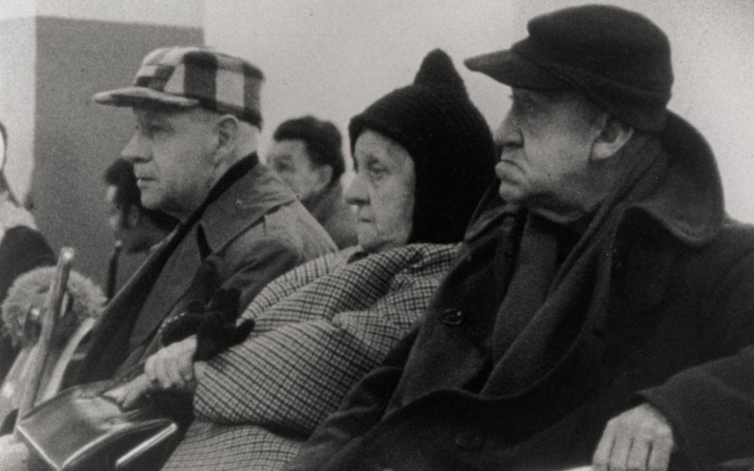 Film still from WELFARE. Three elderly people are sitting in a waiting room.