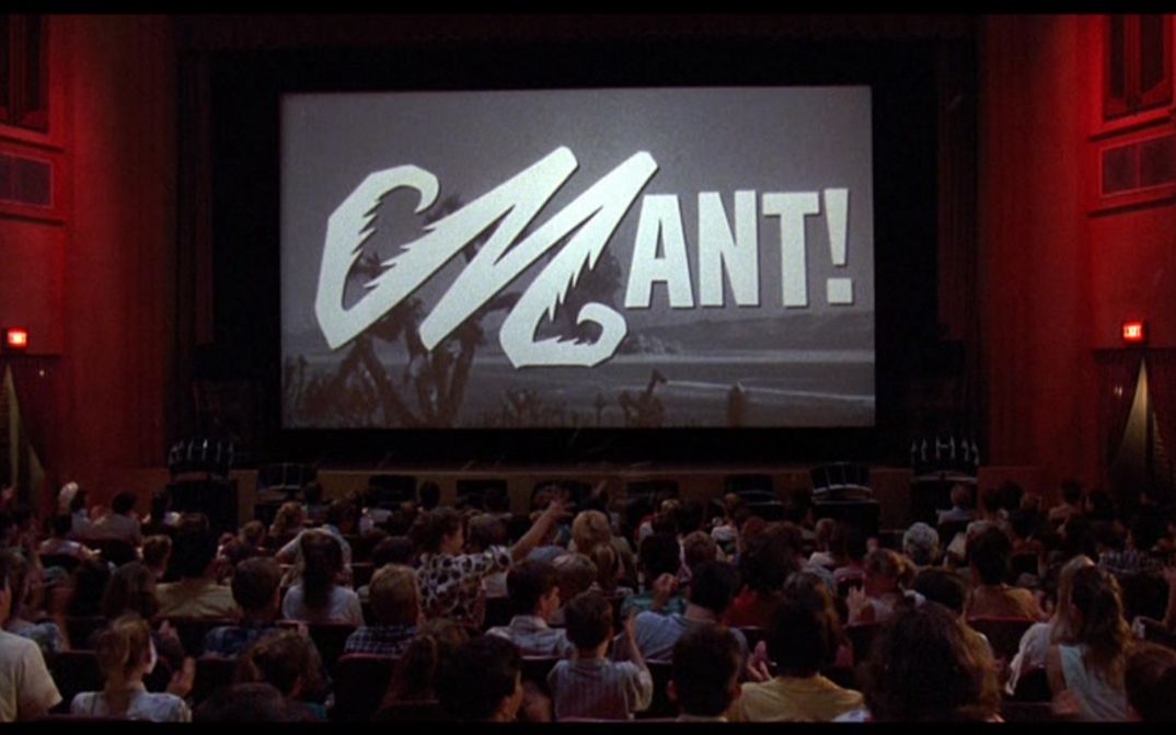Film still from MATINEE: You see a crowded cinema hall, a black and white film is shown on the screen.