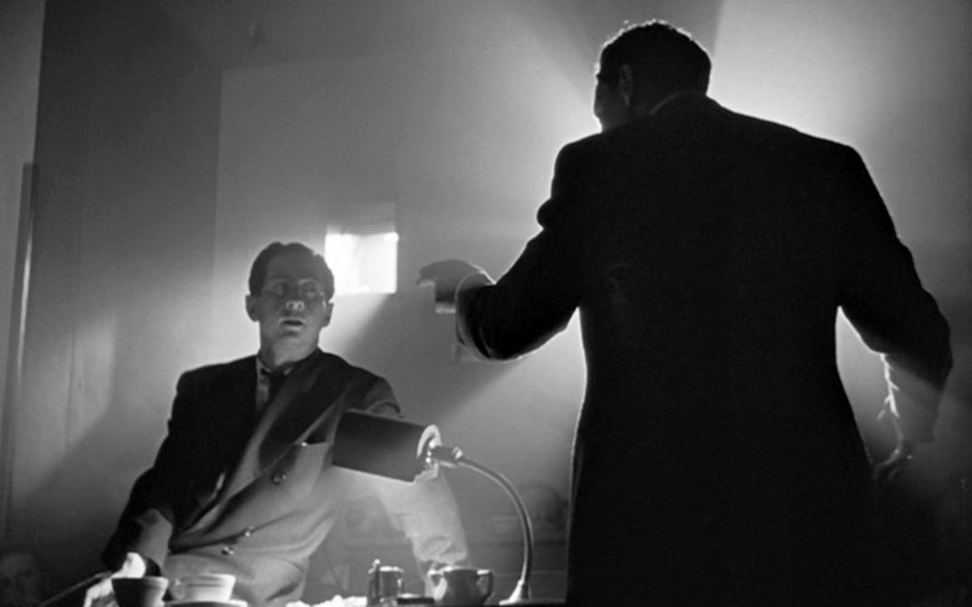 Film still from CITIZEN KANE: Two men are standing at a desk having a discussion. You can only see the back of one of the men.