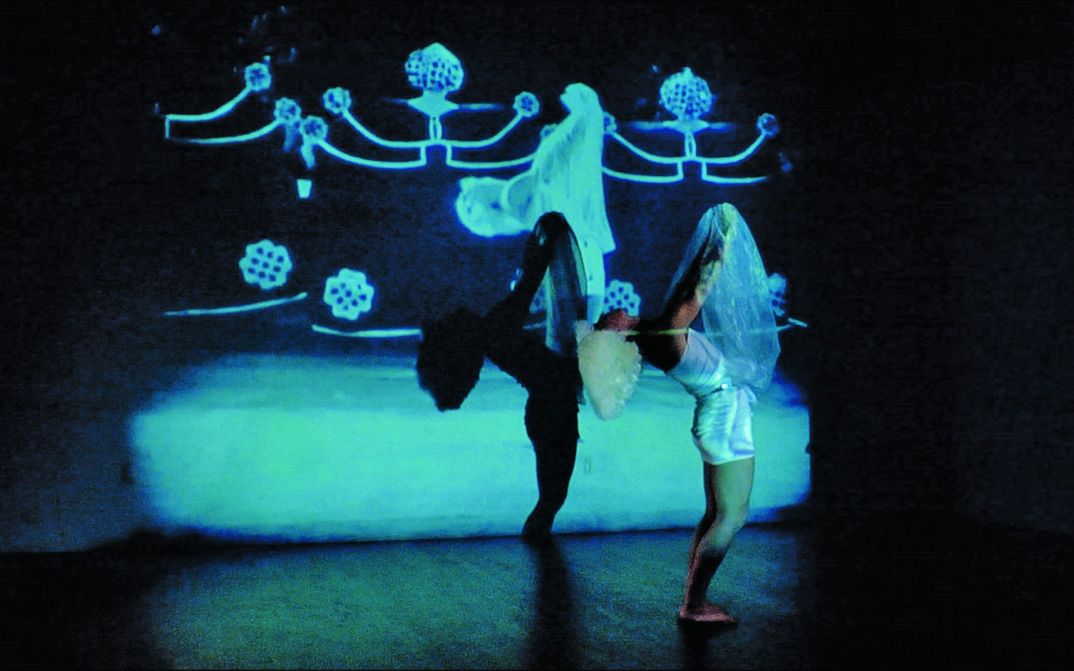 Film still from SALOMANIA: A person dances in front of colorful images projected on the wall.
