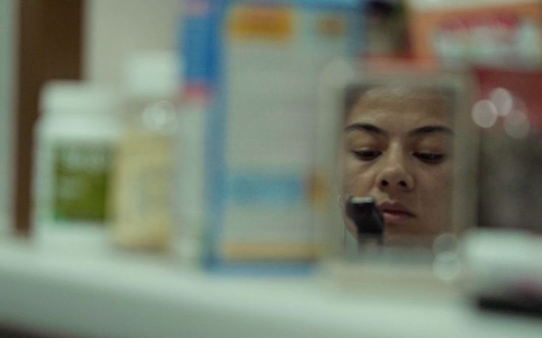Film still from NAGOTA by Sabina Bakaeva. The image shows the reflection of a woman framed by blurred objects.