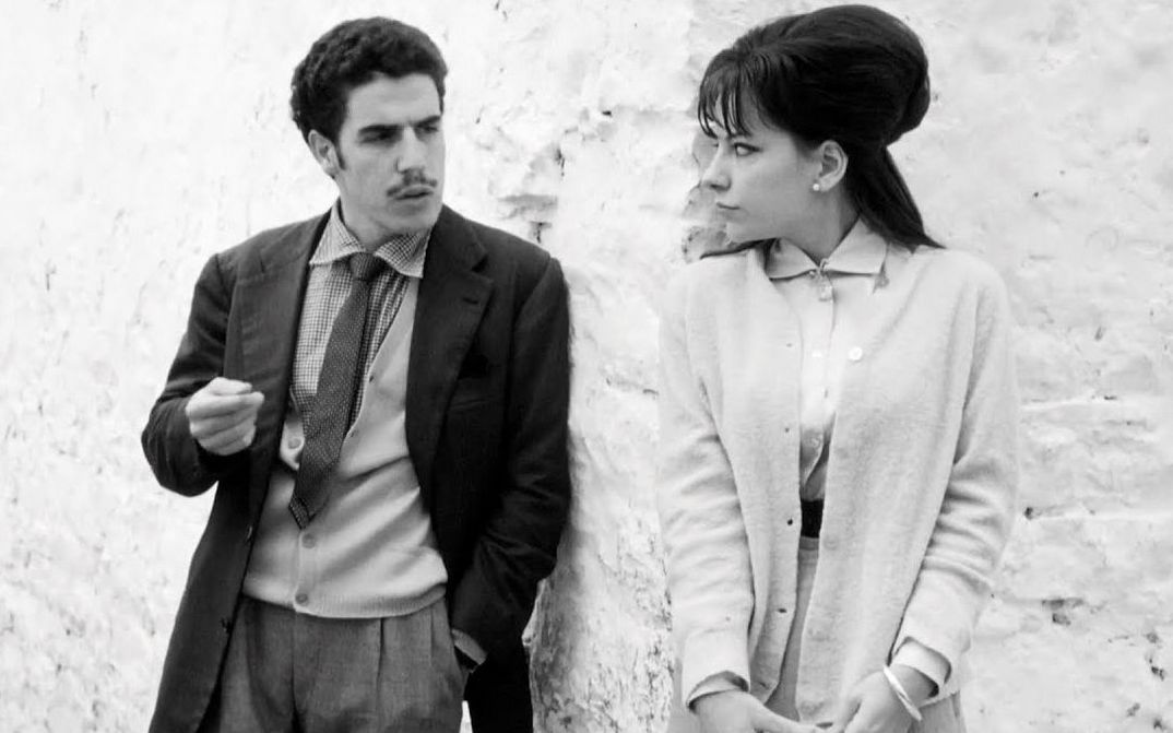 Film still from I BASILISCHI: A man and a woman look at each other leaning against a wall.