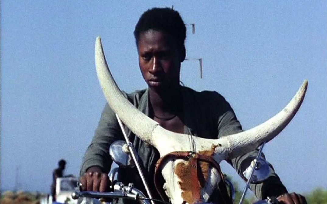 Film still from TOUKI BOUKI: A young person on a motorcycle with a cow