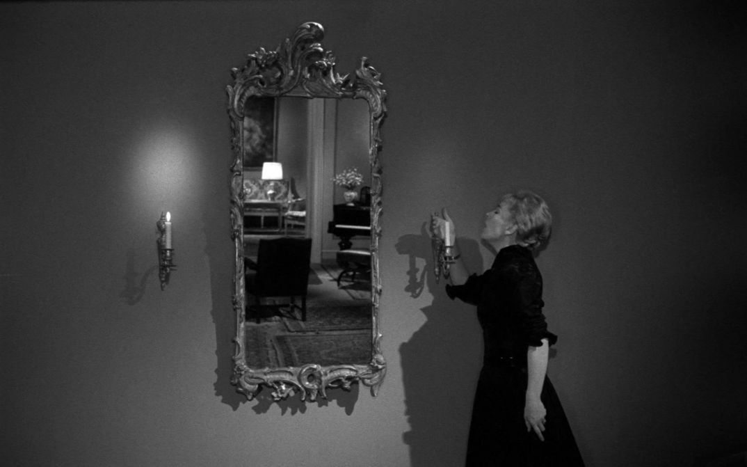 Film still from GERTRUD: A woman blows out a candle hanging next to a mirror.