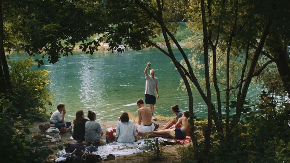 Filmstill aus FÜÜR BRÄNNT: Eine Gruppe junger Menschen feiert am Ufer eines Flusses.