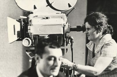 Film still from "Deda-Shvili an rame ar aris arasodes bolomde bneli" by Lana Gogoberidze. It shows a black and white image of a woman using a video camera. 