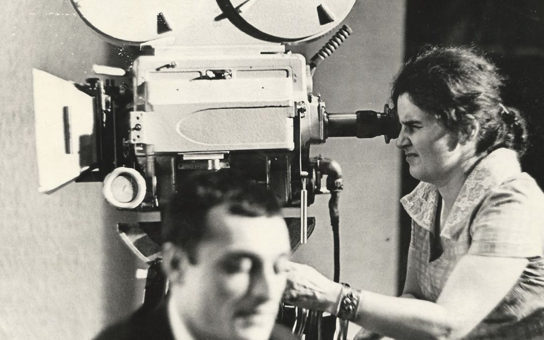 Film still from "Deda-Shvili an rame ar aris arasodes bolomde bneli" by Lana Gogoberidze. It shows a black and white image of a woman using a video camera.