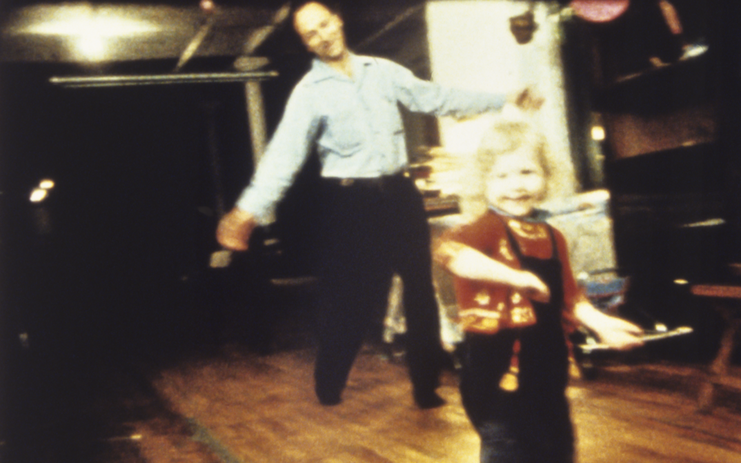Film still from PARADISE NOT YET LOST: Jonas Mekas and a small child dancing in a room.