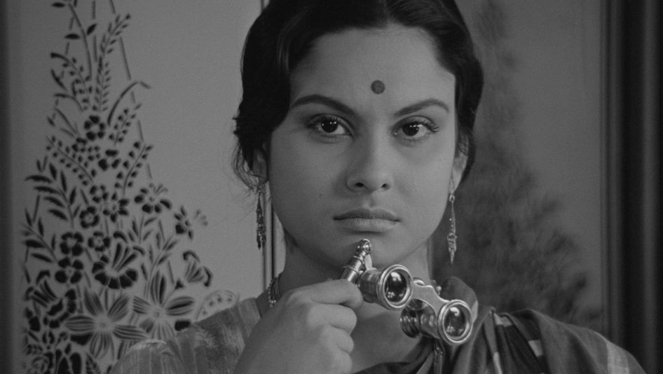 Filmstill from CHARULATA: A woman looks into the camera. She has a dot on her forehead and is holding opera glasses.