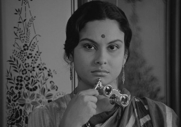 Filmstill from CHARULATA: A woman looks into the camera. She has a dot on her forehead and is holding opera glasses.