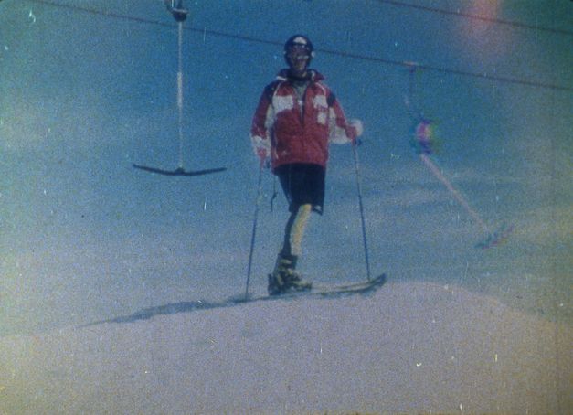 Film still from SCHUSS!: Photograph of a skier in front of a T-bar lift. The image is grainy.