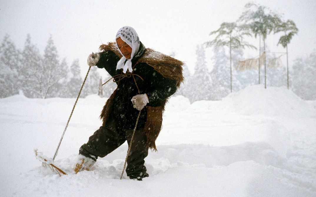 Film still from UNTER SCHNEE: A person in a historical costume walks with snowshoes through a snowy landscape.