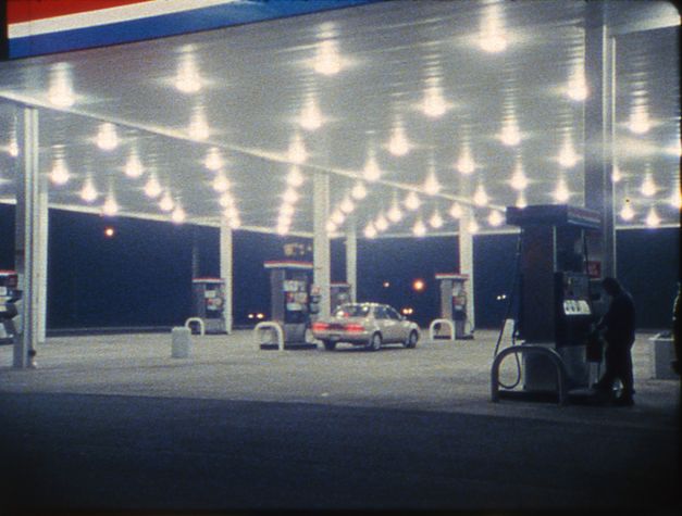 Filmstill from SOMETHING MORE THEN NIGHT: A petrol station in the dark. A car is parked at the petrol pump in the middle.