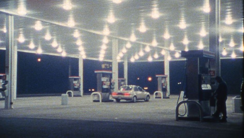 Filmstill from SOMETHING MORE THEN NIGHT: A petrol station in the dark. A car is parked at the petrol pump in the middle.