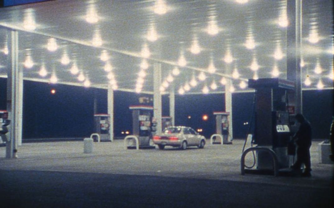 Filmstill from SOMETHING MORE THEN NIGHT: A petrol station in the dark. A car is parked at the petrol pump in the middle.
