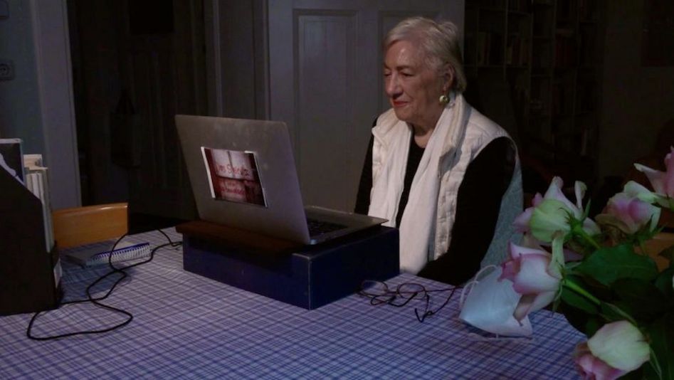 Film still from HELKE SANDER: AUFRÄUMEN: Helke Sander sits at the kitchen table with an open laptop.