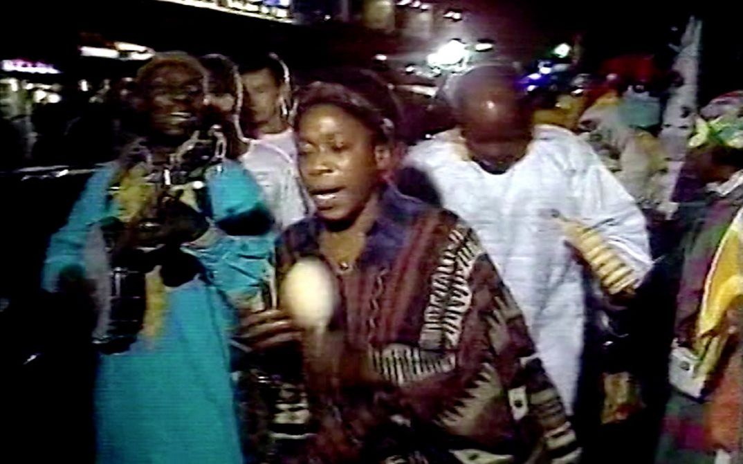 Still from the film "Moune Ô" by Maxime Jean-Baptiste. People walk through a crowded street with musical instruments in their hands.