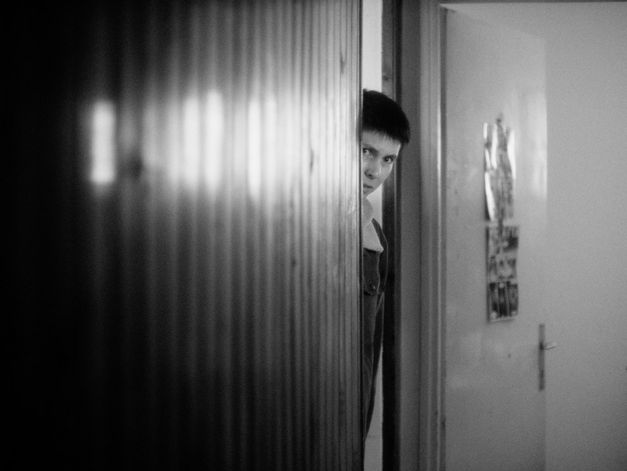 Black and white image of a person looking out of a door frame. 