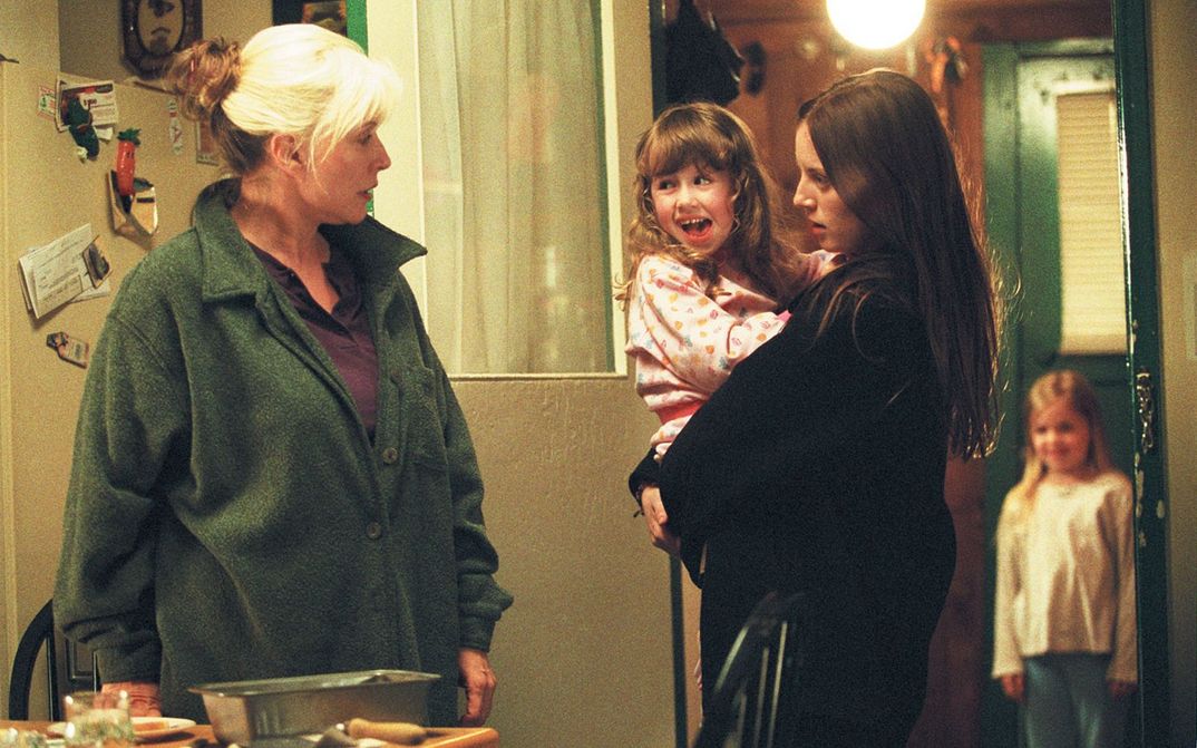 Filmstill from MY LIFE WITHOUT ME: Two women are standing in a living room. One of them is holding a girl in her arms. There is another child in the background.