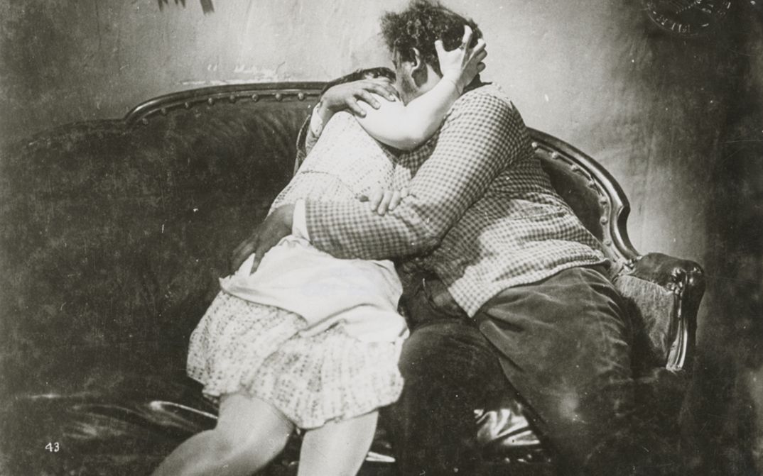 Film still from SO IST DAS LEBEN: A woman and a man kiss and embrace on a sofa.