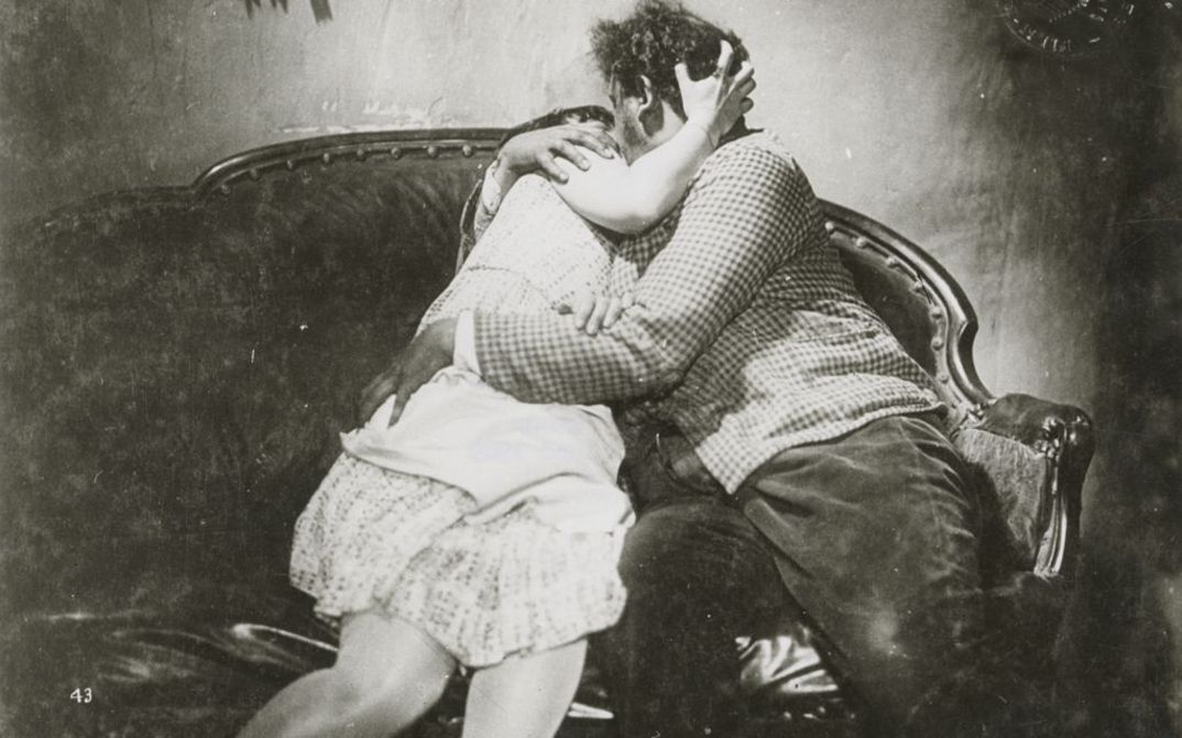 Film still from SO IST DAS LEBEN: A woman and a man kiss and embrace on a sofa.
