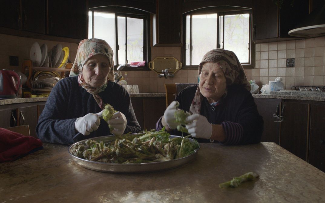 Film still from FORAGERS: Two women sit at a table and clean wild plants.