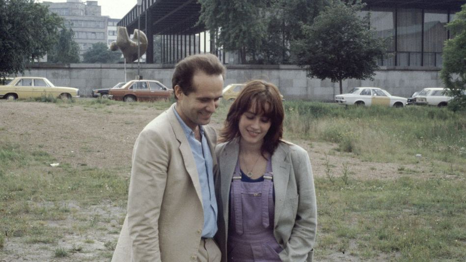 Filmstill aus BERLIN CHAMISSOPLATZ: Ein Mann und eine Frau stehen nah zusammen auf einer Brachfläche vor der Neuen Nationalgalerie in Berlin.