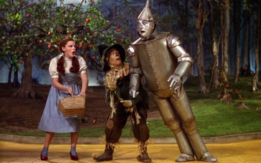 Filmstill aus THE WIZARD OF OZ: Dorothy, die Vogelscheuche und Blechmann auf einem Weg.