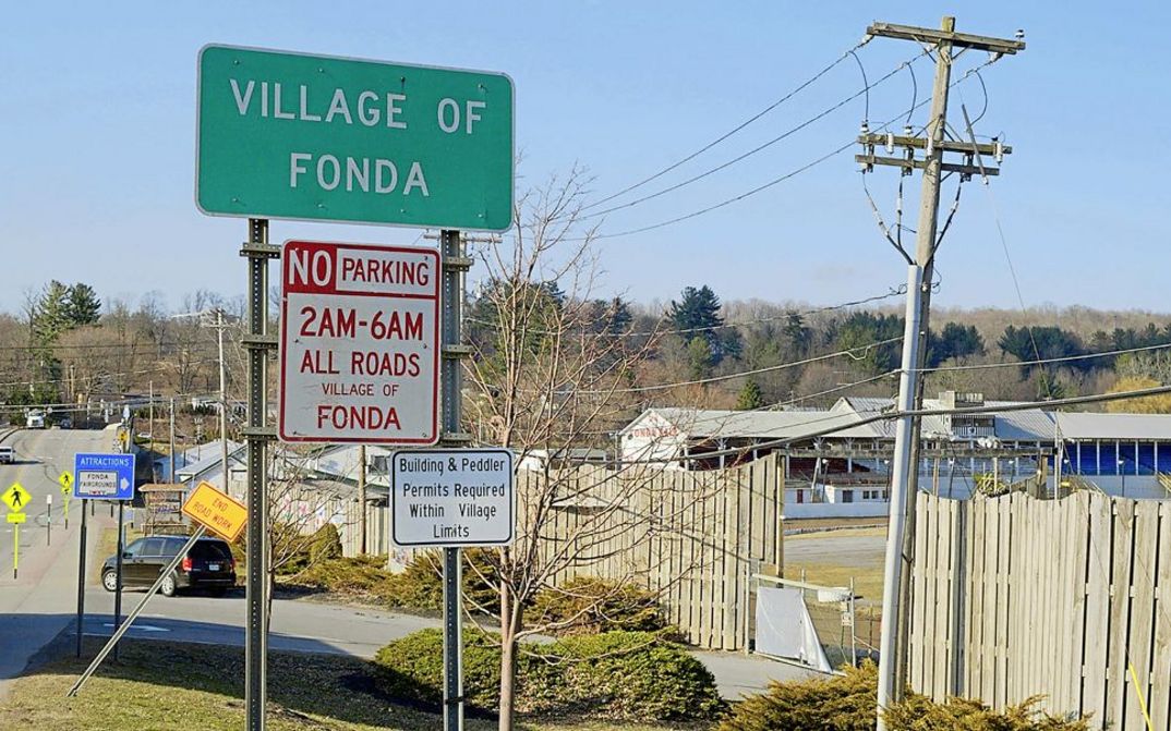 Film still from "Henry Fonda for President " by Alexander Horwath. It shows the entrance sign to the village of Fonda. A road and houses can be seen in the background.