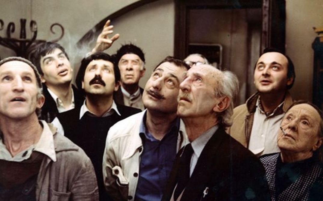 Film still from BLUE MOUNTAINS, OR UNBELIEVABLE STORY: A group of people stand in a room and look up.