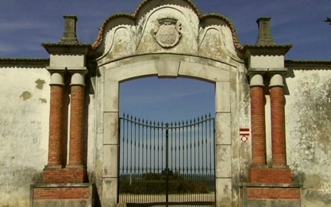 Film still from LINHA VERMELHA: View of an iron gate surrounded by walls.