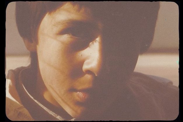 Nahaufnahme eines Jungen, ca. 10-12 Jahre alt, halbes Gesicht im Schatten, warmes Licht, körnige Filmaufnahme.