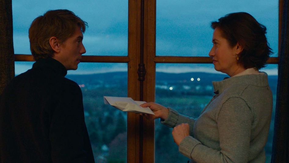 Filmstill from VOUS NE DESIREZ QUE MOI:  Two people are standing in front of the window. The person on the right is holding an envelope out to the other person.