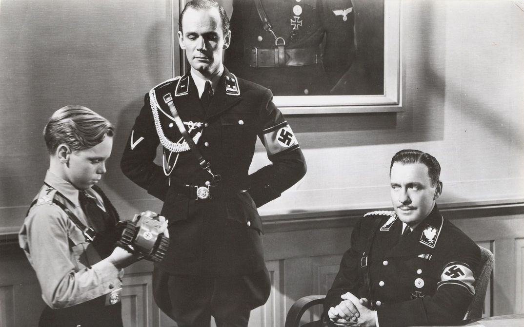 Filmstill aus TO BE OR NOT TO BE: Zwei Wehrmacht-Offiziere mit einem ebenfalls Uniform tragenden Jungen in einem Zimmer.